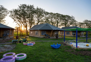 Speelplein met zandbak, speelgoed en safaritenten bij zonsondergang op FarmCamps De Bonte Fries in Friesland.