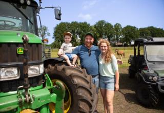 Eine Familie posiert lächelnd vor einem grünen Traktor bei FarmCamps De Bosrand, einem Ferienpark in Drenthe.