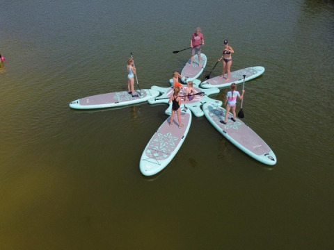 Mehrere Personen stehen auf miteinander verbundenen SUP-Boards auf einem Teich im Ferienpark FarmCamps De Bosrand.