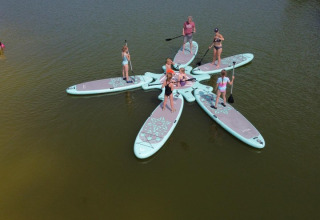 Personas de pie en tablas de paddle interconectadas en forma de flor, sobre un lago en FarmCamps De Bosrand.