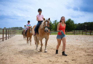 Børn rider på heste med en instruktør i sandet på FarmCamps De Bosrand, en feriepark i Drenthe, Holland.