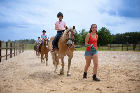Kinder reiten mit einer Lehrerin auf Pferden im Sand bei FarmCamps De Bosrand, einem Ferienpark in Drenthe.