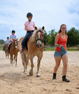 Niños montando a caballo con una instructora en FarmCamps De Bosrand, un parque vacacional en Drenthe, Países Bajos.