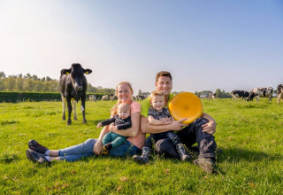 Una familia sentada en el césped de FarmCamps De Buitenhoeve, Gelderland, Países Bajos, rodeada de vacas y queso.