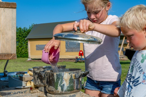 Due bambini giocano all’aperto a FarmCamps De Buitenhoeve, Gelderland, Paesi Bassi, versando acqua nelle pentole.