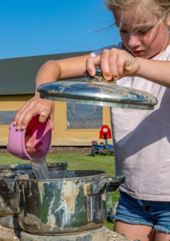 Zwei Kinder spielen draußen bei FarmCamps De Buitenhoeve in Gelderland, Niederlande, mit Töpfen und Wasser.
