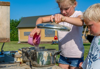 Zwei Kinder spielen draußen bei FarmCamps De Buitenhoeve in Gelderland, Niederlande, mit Töpfen und Wasser.