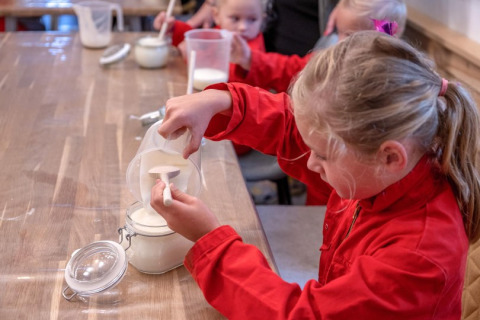 Kinder in roten Overalls messen Mehl ab bei FarmCamps De Buitenhoeve in Gelderland, Niederlande.