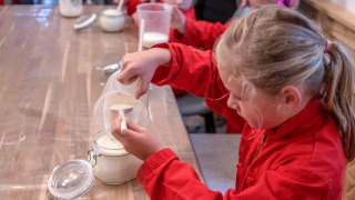 Kinder in roten Overalls messen Mehl ab bei FarmCamps De Buitenhoeve in Gelderland, Niederlande.