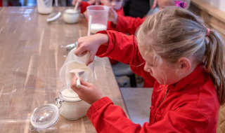 Children in red overalls scoop flour during a hands-on activity at FarmCamps De Buitenhoeve, Gelderland.