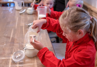 Kinderen in rode overall scheppen meel bij een activiteit op FarmCamps De Buitenhoeve, Gelderland.