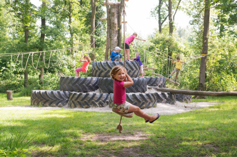 Children playing on a playground with giant tractor tires and ropes at FarmCamps De Geele Bosch, Friesland.