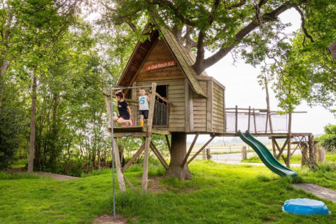 Niños juegan en una casita del árbol con tobogán en FarmCamps De Geele Bosch en Frisia, Países Bajos.
