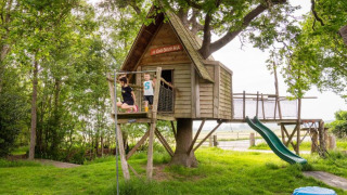 Niños juegan en una casita del árbol con tobogán en FarmCamps De Geele Bosch en Frisia, Países Bajos.