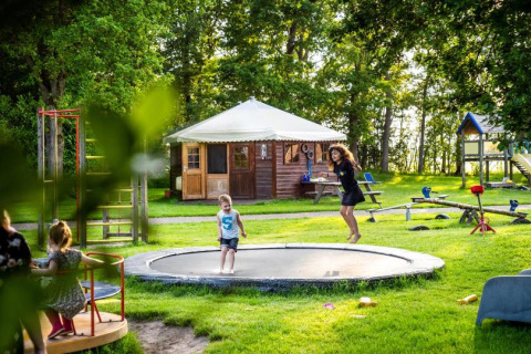 Kinder spielen auf einem Spielplatz mit Trampolin bei FarmCamps De Geele Bosch, Ferienpark in Friesland, Niederlande.