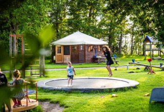 Kinder spielen auf einem Spielplatz mit Trampolin bei FarmCamps De Geele Bosch, Ferienpark in Friesland, Niederlande.