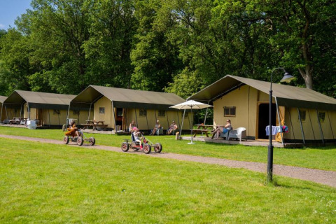 Kinder fahren Kettcars vor Glamping-Zelten im Ferienpark FarmCamps De Geele Bosch in Friesland, Niederlande.