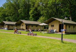 Kinder fahren Kettcars vor Glamping-Zelten im Ferienpark FarmCamps De Geele Bosch in Friesland, Niederlande.