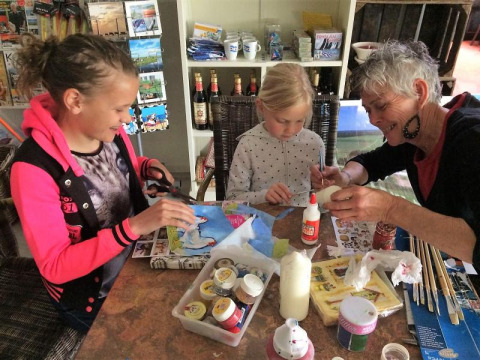 Niños y una adulta creando manualidades en una mesa en FarmCamps De Geele Bosch, Friesland, Países Bajos.