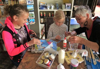 Børn og en voksen laver håndværksprojekter sammen ved et bord på FarmCamps De Geele Bosch i Friesland.