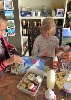Niños y una adulta creando manualidades en una mesa en FarmCamps De Geele Bosch, Friesland, Países Bajos.