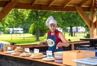 Kvinde i kokkehue serverer pandekager udendørs på FarmCamps De Geele Bosch i Friesland, Holland.