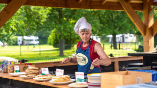 Mujer con gorro de chef sirviendo panqueques al aire libre en FarmCamps De Geele Bosch, Friesland, Países Bajos.