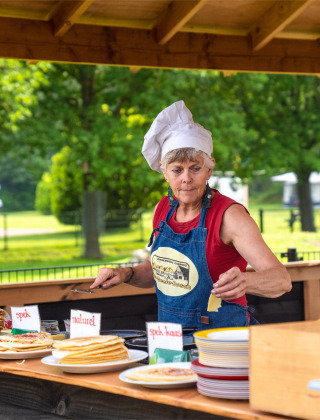 Mujer con gorro de chef sirviendo panqueques al aire libre en FarmCamps De Geele Bosch, Friesland, Países Bajos.