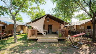 Safari-Zelt Villatent Outback mit Veranda und Hängematte, umgeben von Bäumen und Sonnenschein.