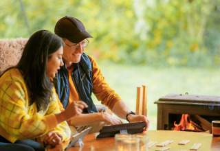 Two people enjoy a board game and fireplace at RØSTIG Dorst, a holiday park in North-Brabant, Netherlands.