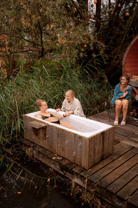 Tres mujeres disfrutan de una bañera al aire libre rodeada de naturaleza en el parque vacacional RØSTIG Dorst.
