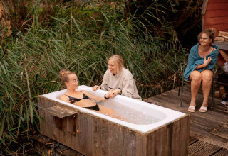 Tres mujeres disfrutan de una bañera al aire libre rodeada de naturaleza en el parque vacacional RØSTIG Dorst.