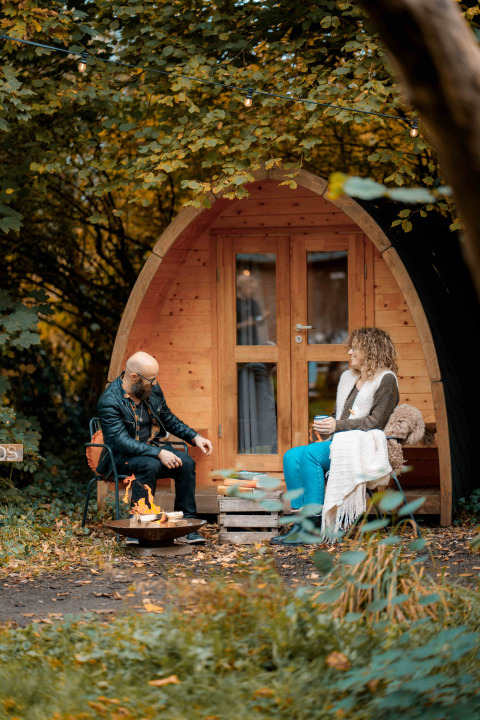 Dos personas se relajan junto a una cabaña de madera en el bosque en RØSTIG Dorst, un parque vacacional en Brabante Septentrional, Países Bajos.