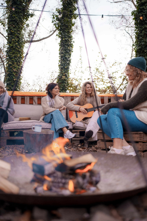 Frauen sitzen an einem Lagerfeuer, eine spielt Gitarre, Ferienpark RØSTIG Dorst, Nord-Brabant, Niederlande.