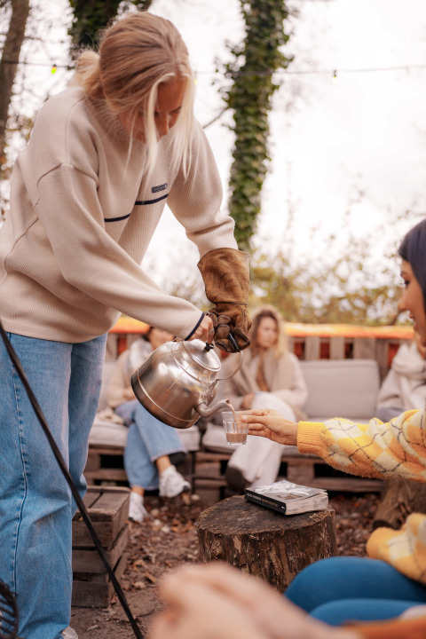 Person pouring hot drink outdoors at RØSTIG Dorst holiday park in North-Brabant, Netherlands.