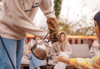 Person pouring hot drink outdoors at RØSTIG Dorst holiday park in North-Brabant, Netherlands.