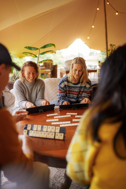 Four people enjoy playing a board game together in a cozy tent at RØSTIG Dorst holiday park, Netherlands.