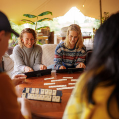 Vier Freunde spielen ein Brettspiel und lachen zusammen in einem Zelt im Ferienpark RØSTIG Dorst.