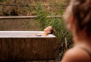 Deux femmes se détendent près d’une baignoire extérieure entourée de nature au RØSTIG Dorst, Pays-Bas.