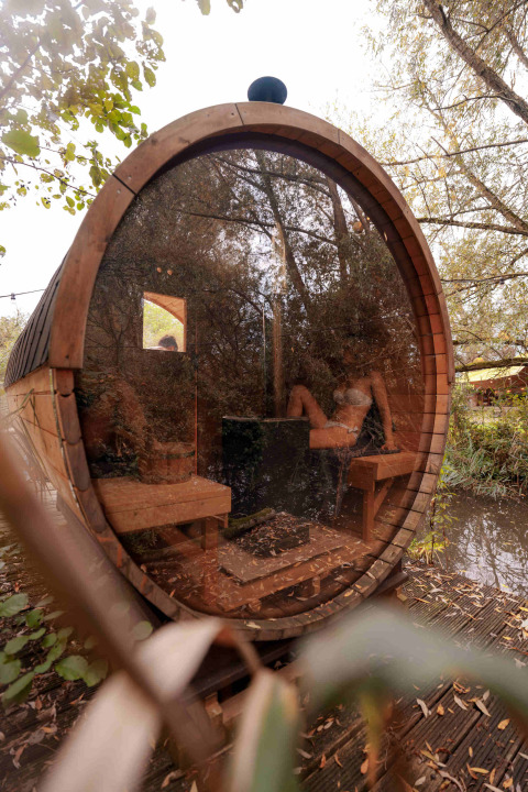 Sauna circular de madera con frente de cristal en RØSTIG Dorst, rodeado de naturaleza en North Brabant, Países Bajos.