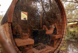 Ronde houten sauna met glazen voorkant bij vakantiepark RØSTIG Dorst, omgeven door natuur in Noord-Brabant.