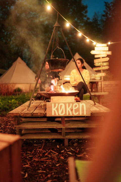 Abendliche Szene mit Lagerfeuer und Kessel bei RØSTIG Dorst Ferienpark, Nordbrabant, Niederlande.