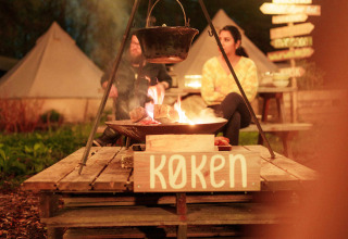 Avondkampvuur met hangpot en mensen aan het ontspannen in RØSTIG Dorst vakantiedomein, Nederland.