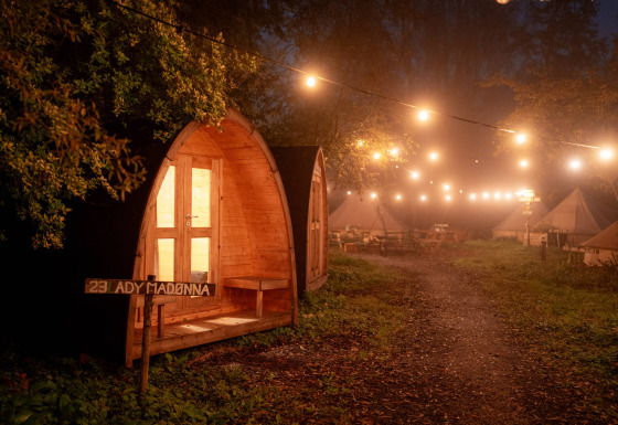 Lit wooden cabin and tents at night with string lights at RØSTIG Dorst holiday park, North-Brabant, Netherlands.
