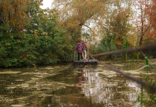 Twee personen staan op een vlot aan een vijver omringd door herfstbomen in RØSTIG Dorst, Nederland.