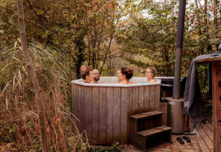 Vier mensen genieten van een buiten bubbelbad in vakantiepark RØSTIG Dorst in Noord-Brabant, Nederland.