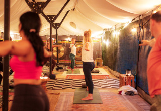 Persone partecipano a una lezione di yoga sotto una tenda illuminata al parco RØSTIG Dorst, Brabante.