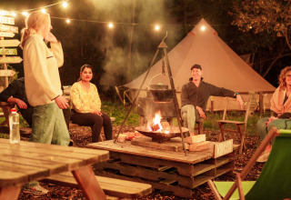 Menschen sitzen bei einem Lagerfeuer und Lichterketten im RØSTIG Dorst Ferienpark, Nordbrabant.