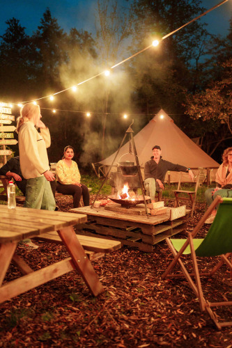People gather around a campfire under string lights at RØSTIG Dorst holiday park in North Brabant.