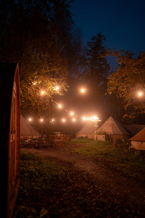 Zona de glamping al anochecer en RØSTIG Dorst, Países Bajos, con luces colgantes y tiendas de campaña.